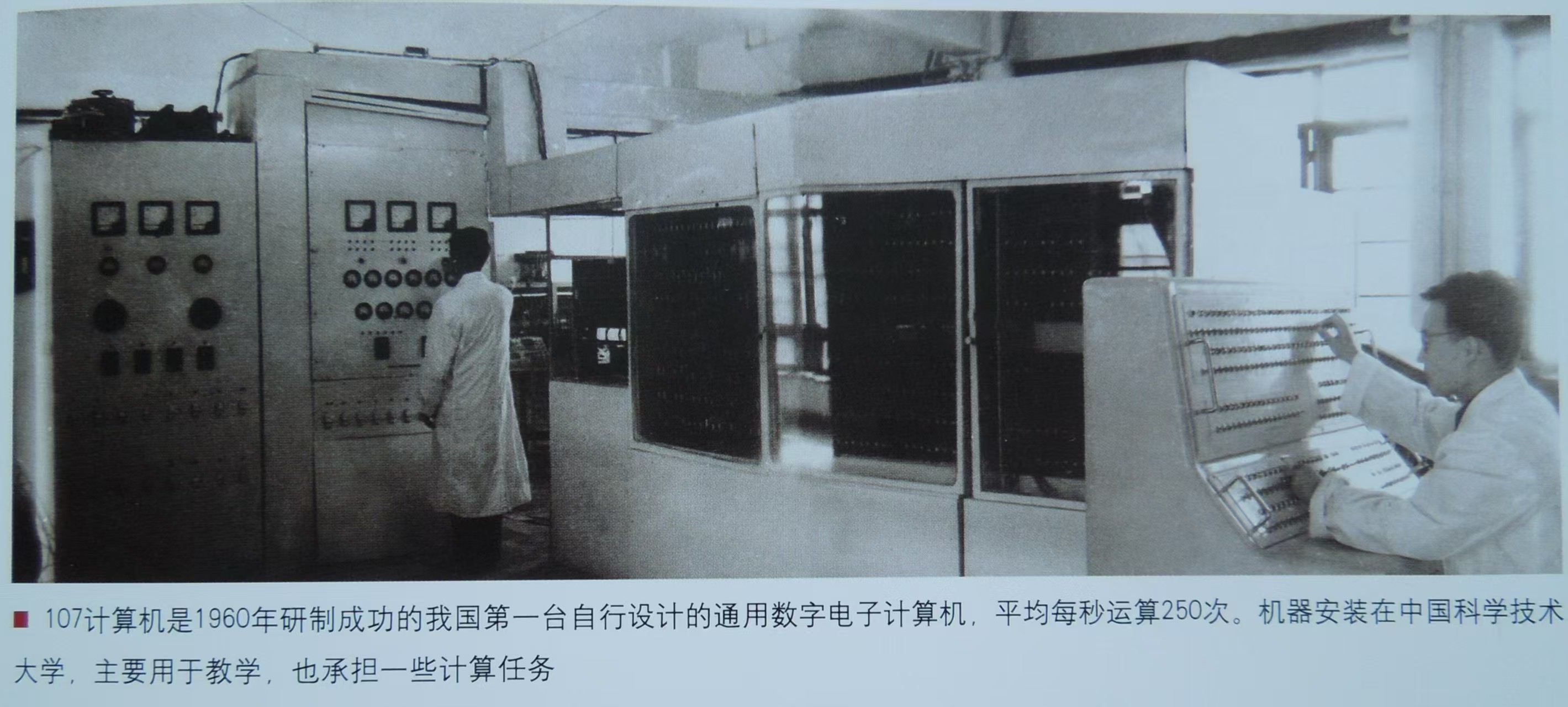 宽幅机房里，电源柜、开放机架与控制台依次展开，两位工作人员一站一坐。